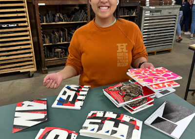 A student smiles, holding a stack of wood type prints in the Hamilton Wood Type Museum printing room.