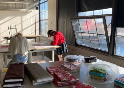 Two students work cutting fabric in a sunny classroom.