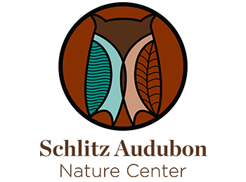 A circular logo sits above the words "Schlitz Audubon Nature Center." The circle is a reddish brown color and includes a stylized icon of an owl with two wing shapes - one is teal and has wavy lines representing water, and the other is reddish-brown with vein lines that make it resemble a leaf.